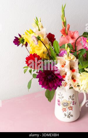 Un vase contient une variété de fleurs fraîches avec différentes couleurs. Les fleurs sont placées sur une table rose. Derrière le vase se trouve un mur Uni dans un roo lumineux Banque D'Images