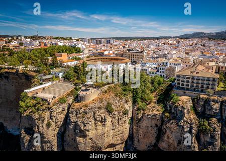 Vue aérienne d'une ville à flanc de falaise avec des bâtiments blancs, des toits en terre cuite et des arbres luxuriants perchés au-dessus d'un canyon spectaculaire, Ronda, Espagne Banque D'Images