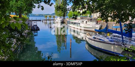 Uberlingen, Allemagne - 07 juillet 2024. Un port pittoresque encadré par des feuilles d'arbre vertes avec plusieurs bateaux sur le lac de Constance dans la matinée. Banque D'Images