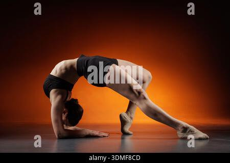 Vue latérale d'une femme flexible faisant l'étirement du dos de l'avant-bras sur le sol du studio avec un fond dégradé orange et un espace de copie pour la bannière du site de fitness o Banque D'Images