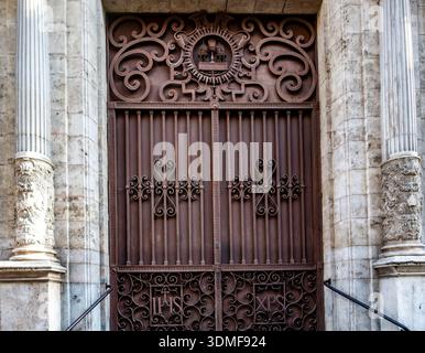 Porte complexe en fer forgé foncé à l'entrée d'un bâtiment historique de Valence, en Espagne, ornée de symboles religieux et de motifs de volutes ornés. Banque D'Images
