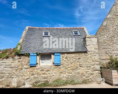 Une maison rustique en pierre avec de charmants volets bleus se dresse sous un ciel bleu clair, évoquant la beauté intemporelle de la vie de la campagne méditerranéenne. Banque D'Images
