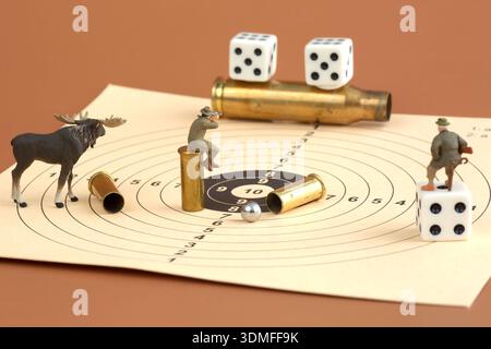 Des chasseurs miniatures et des orignaux disposés sur une cible de tir avec des munitions et des dés dans une nature morte conceptuelle. Banque D'Images