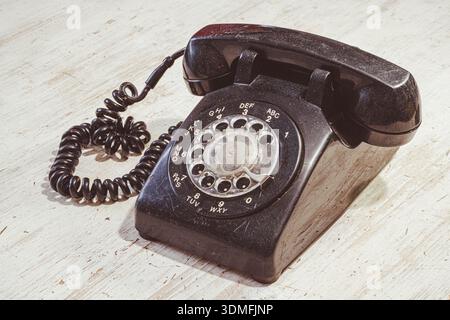 Un téléphone rotatif est assis sur une table en bois. Le téléphone a un corps noir et un cordon enroulé. L'arrière-plan montre une surface en bois clair qui met en évidence Banque D'Images