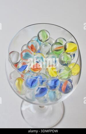Photographie de haute qualité d'une tasse en verre remplie de billes avec des centres colorés, placée sur une table blanche propre. Parfait pour la photographie de produits, Banque D'Images