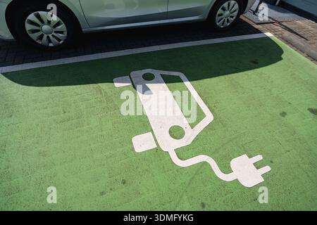 Symbole de charge de véhicule électrique peint sur la chaussée verte marquant un espace de stationnement désigné pour véhicule électrique Banque D'Images