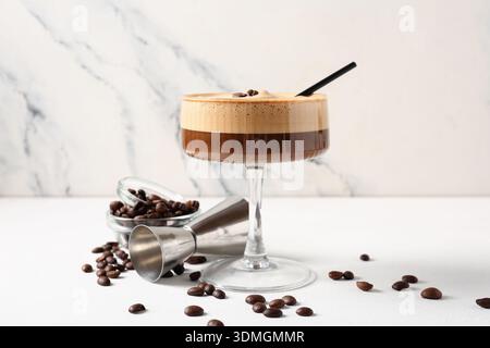 Verre de savoureux cocktail espresso martini et grains de café sur la table blanche près du mur de marbre, gros plan Banque D'Images