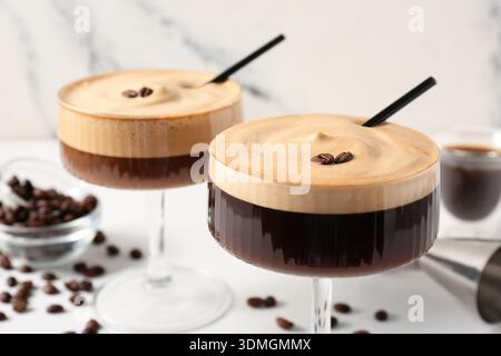 Verres de délicieux cocktail espresso martini et grains de café sur la table blanche près du mur de marbre, gros plan Banque D'Images