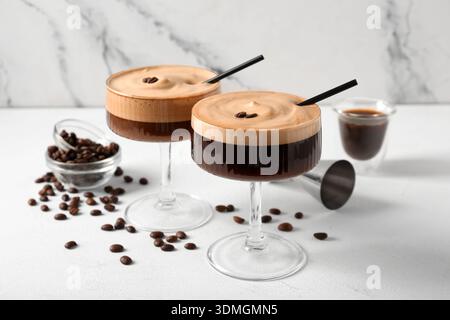 Verres de délicieux cocktail espresso martini et grains de café sur la table blanche près du mur de marbre, gros plan Banque D'Images