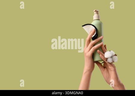 Mains féminines tenant le tampon réutilisable, bouteille de produit cosmétique et fleur de coton sur fond vert Banque D'Images
