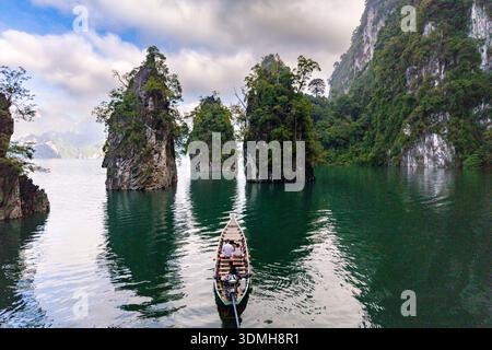 Découvrez les paysages à couper le souffle du parc national de Khao Sok en Thaïlande avec des eaux émeraude reflétant d'imposantes falaises calcaires. Un bateau traditionnel Banque D'Images