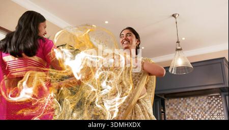 Femme dansante en saree or jaune pâle tourbillonnant à la cuisine à la maison, avec saree rose, lampe suspendue Banque D'Images
