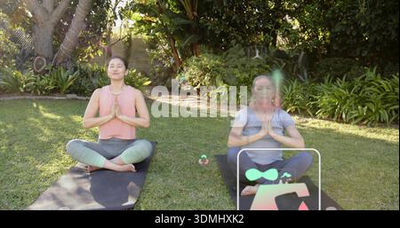Méditer deux femmes assises dans le jardin de l'arrière-cour dans des vêtements de yoga sur des tapis noirs avec superposition numérique Banque D'Images