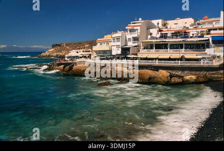 Bleu brillant, journée ensoleillée brillante avec des vagues d'eau de l'océan en mouvement le long de la ville côtière idyllique, îles Canaries, la Caleta, Tenerife, Espagne. Banque D'Images