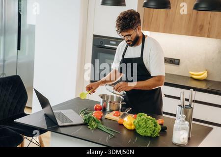En tablier noir. Bel homme prépare de la nourriture dans la cuisine. Banque D'Images