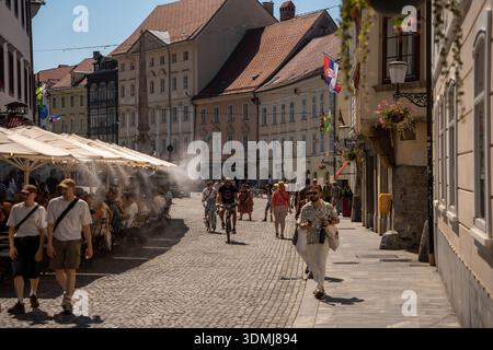 Ljubljana, Slovénie - 10 août 2025 : une place animée de Ljubljana avec des sièges de café en plein air avec la brume rafraîchissante, l'architecture historique et les gens Banque D'Images