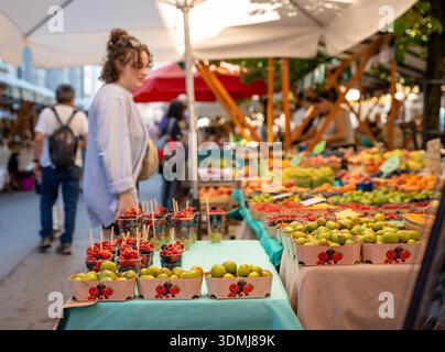 Ljubljana, Slovénie - 10 août 2025 : une jeune femme parcourt un marché en plein air coloré à Ljubljana, où les figues fraîches et les tasses de baies mélangées sont n° Banque D'Images