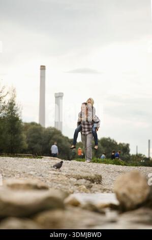 Jeune couple s'amusant avec un piggyback ride urbain Riverside. Banque D'Images