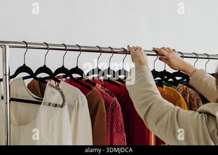 La femme organise une tenue professionnelle dans l'ordre arc-en-ciel sur les cintres Banque D'Images