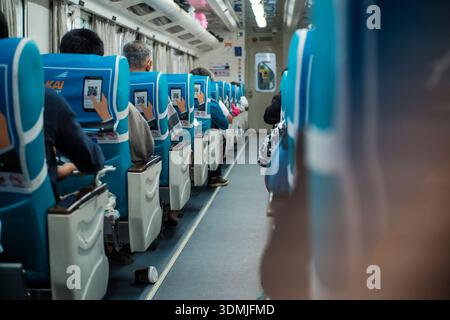 Une longue photo capture l'intérieur d'un train, montrant des rangées de sièges bleus occupés par des passagers. L'allée est visible, menant vers l'avant du Banque D'Images