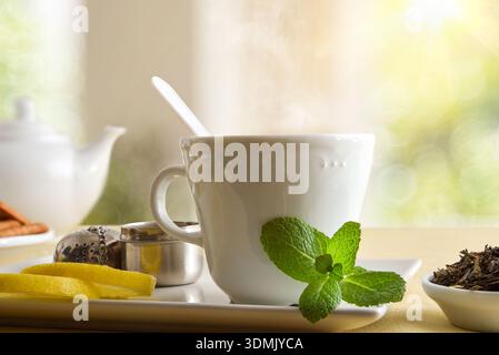 Macro détail d'une tasse de thé sur une soucoupe en céramique à la menthe et au citron dans un salon. Vue de face. Banque D'Images
