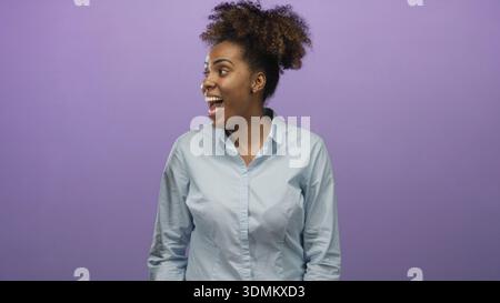 Femme riant avec la bouche ouverte et le visage visible, tournant la tête vers la gauche et faisant des gestes d'une main dans un studio violet ; joie optimisme. Banque D'Images