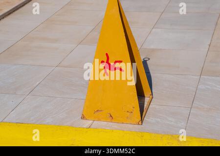 Un panneau d'avertissement jaune avec un symbole de figure rouge avertit d'un risque de glissade sur une surface carrelée adjacente à une ligne peinte en jaune Banque D'Images