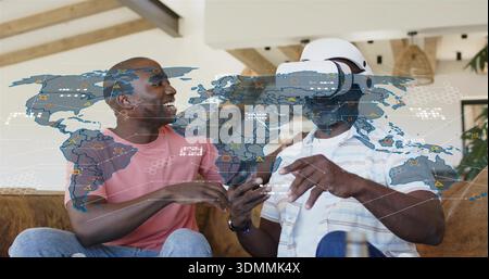 Homme souriant en chemise rose guidant homme portant VR dans le salon, avec smartphone et hologramme Banque D'Images