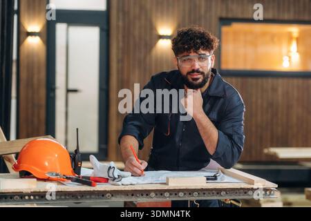 Expression faciale joyeuse. Portrait d'un menuisier masculin posant dans un atelier de menuiserie. Banque D'Images