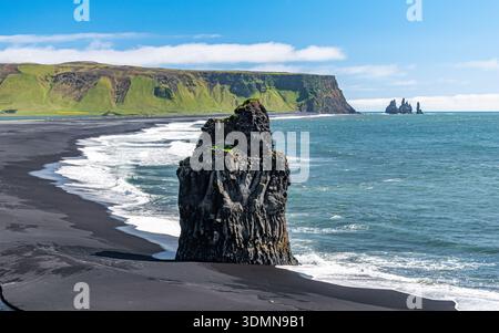 Arnardrangur, une pile de basalte située sur le sable noir de la plage de Reynisfjara près de Vik dans le sud de l'Islande, avec des piles de Reynisdrangar à l'arrière Banque D'Images