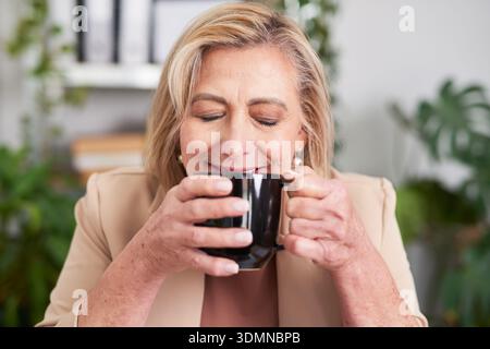 Femme d'affaires confiante appréciant le café dans le bureau, souriant tout en sirotant de Mug Banque D'Images