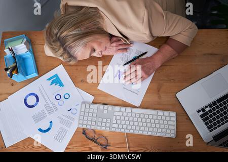 Femme d'affaires analysant des documents au bureau avec des graphiques, un ordinateur portable et un clavier sur une surface en bois Banque D'Images