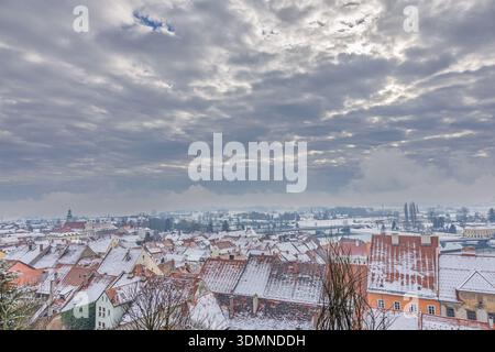 Une vue panoramique sur un village enneigé avec des maisons colorées et des toits rouges sous un ciel spectaculaire et rempli de nuages. Calme hivernal, rues tranquilles, a Banque D'Images