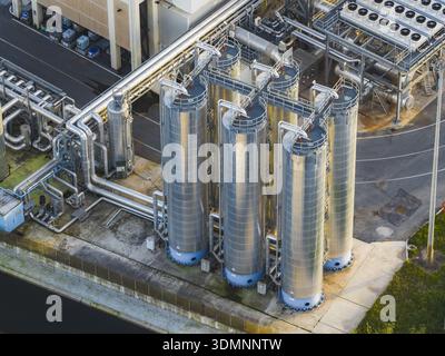 Vue aérienne de réservoirs industriels brillants sous la lumière du soleil, reliés entre eux par un réseau de tuyaux, projetant des ombres sur le béton ci-dessous, Rome, Latium, Banque D'Images