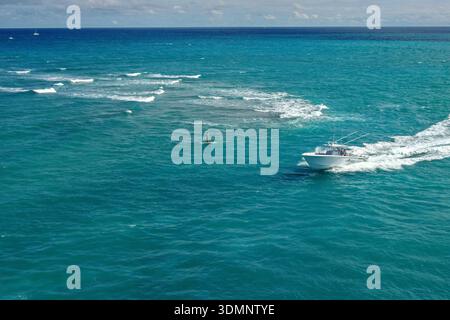 Vue aérienne d'un bateau coupant dans les eaux turquoises, contrastant avec le sillage blanc, près d'une figure solitaire debout sur une planche à paddles, Jupiter Banque D'Images