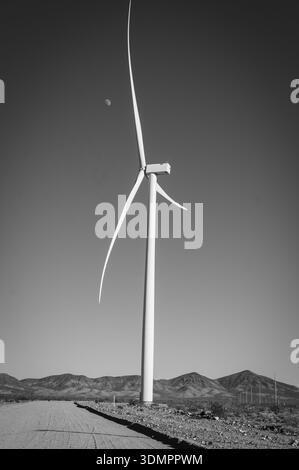 Un moulin à vent électrique géant avec la lune montrant à travers ses pales. Un parc éolien solaire entre Kingman AZ et Las Vegas Nevada. Noir a Banque D'Images