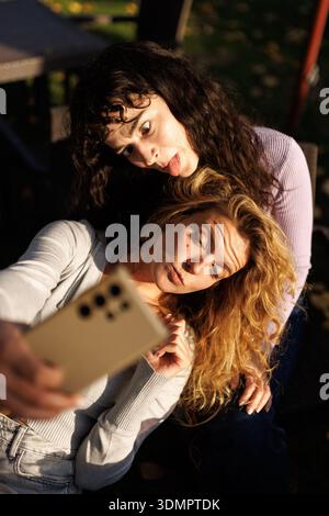 Deux amis faisant des visages stupides tout en prenant un selfie dans un cadre extérieur lumineux pendant l'heure dorée Banque D'Images