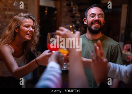 Groupe d'amis toast avec des boissons et souriant dans une réunion intérieure décontractée Banque D'Images
