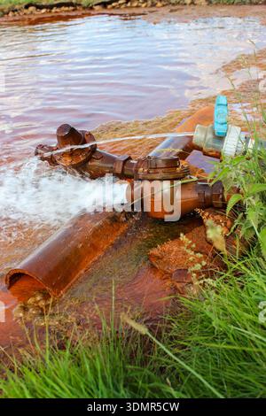 Un vieux robinet rouillé à partir duquel un lac artificiel est rempli. Sédiments rouillés au fond du lac. Un tuyau d'où s'écoule l'eau propre. Banque D'Images