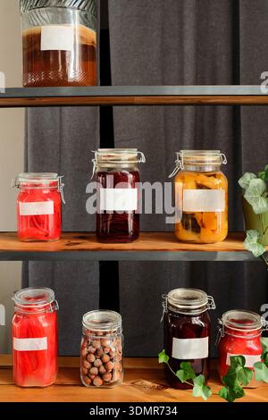 Collection de bocaux en verre remplis d'aliments fermentés et conservés maison, disposés sur des étagères en bois rustiques. Étiquettes vierges, couleurs naturelles et Gree Banque D'Images