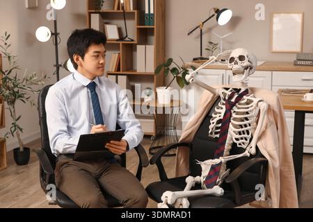 Jeune homme d'affaires asiatique avec squelette humain travaillant dans le bureau Banque D'Images