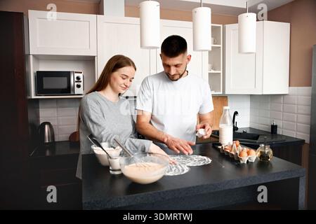 Deux personnes se tiennent debout dans une cuisine pour préparer un repas. Ils travaillent ensemble avec des bols et des ingrédients sur un comptoir. Il est le matin, et ils ont l'air heureux comme t Banque D'Images