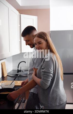 Un homme et une femme préparent le petit déjeuner dans une cuisine. La femme embrasse l'homme par derrière comme il cuisine, créant une atmosphère chaleureuse et confortable pendant Banque D'Images