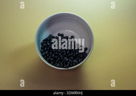Vue de dessus minimaliste de bleuets frais dans un bol blanc sur fond beige. Snack sain aux baies avec espace de copie. Banque D'Images