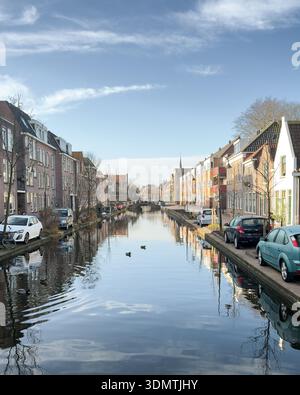 Vue symétrique d'un canal hollandais bordé de maisons traditionnelles, de reflets d'eau calmes et d'un ciel dégagé. Banque D'Images