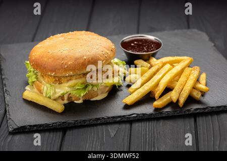 Hamburger de poulet croustillant avec laitue et sauce au fromage fondu, frites et ketchup, fond foncé Banque D'Images