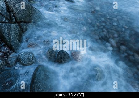 Les vagues se déplacent sur les pierres le long de la côte suédoise pendant la soirée. L'eau coule sur les rochers créant une texture lisse et un mouvement doux. Banque D'Images
