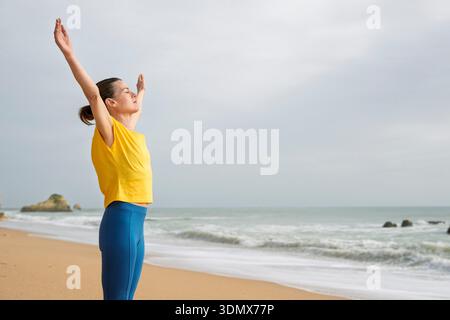 femme debout sur la plage avec les bras larges, les yeux fermés, embrassant la brise Banque D'Images
