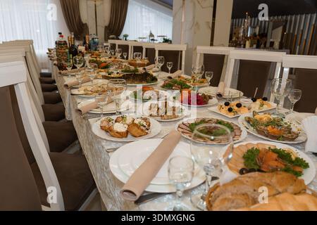 Une longue table de banquet magnifiquement agencée avec des draps blancs, de la vaisselle fine, et une abondance de plats gastronomiques, y compris du poisson, des salades et des pâtisseries, Banque D'Images