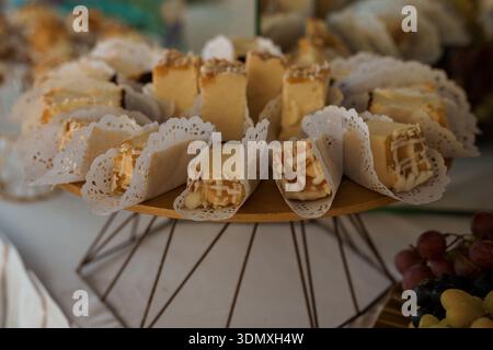 Un plateau de fromages magnifiquement arrangé avec des fromages assortis enveloppés dans de délicats papiers, exposé sur un stand en bois avec des raisins à proximité, ide Banque D'Images